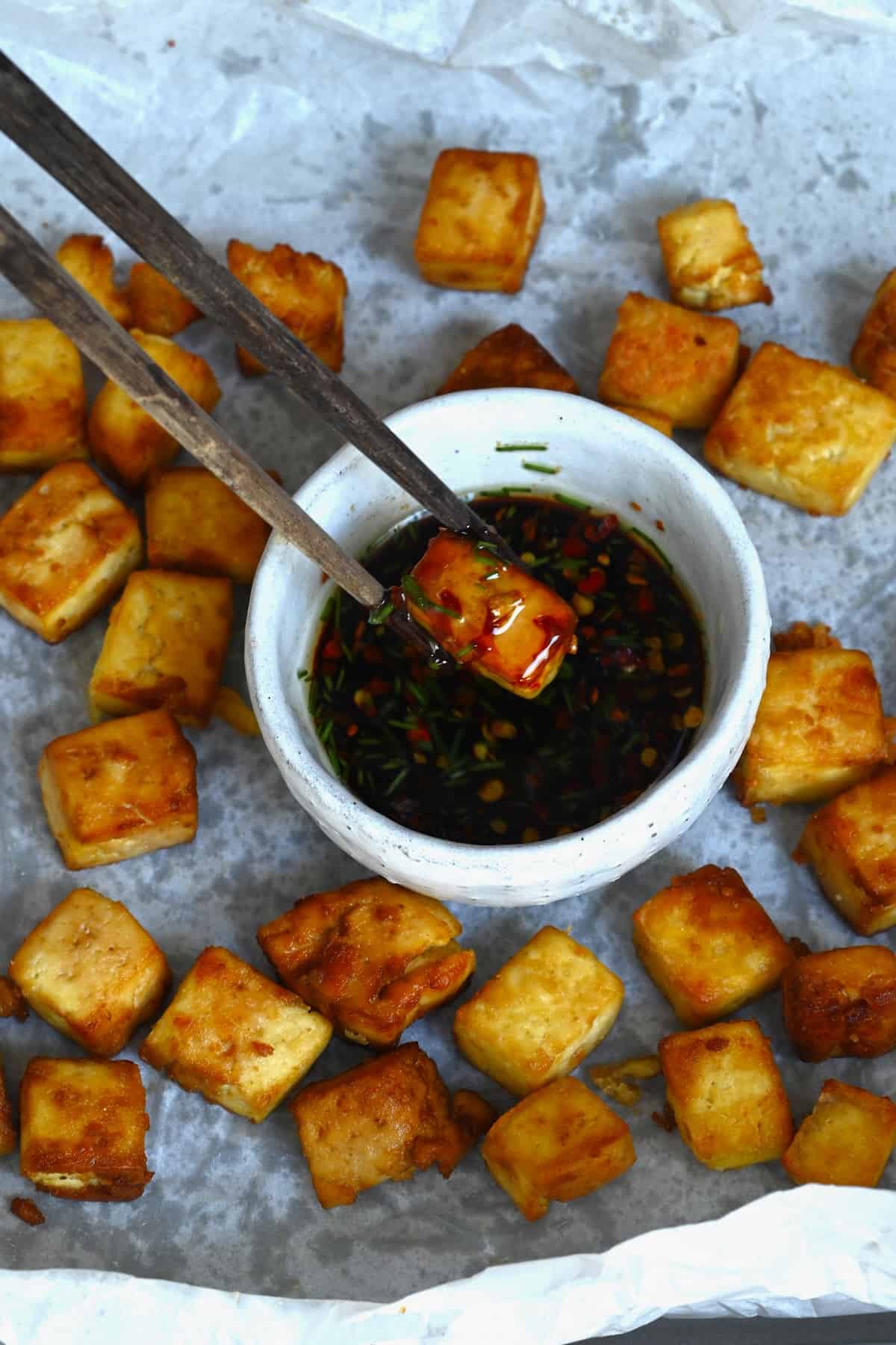 Dipping crispy tofu cube in soy sauce
