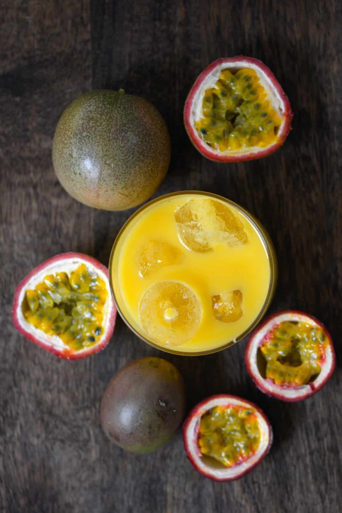 A glass with passion fruit juice and several passion fruit aroun dit