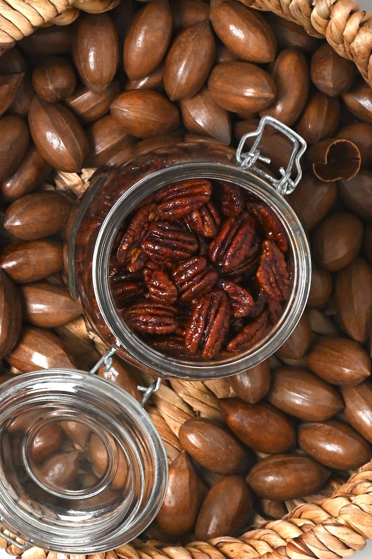 A jar filled with homemade candied pecans over pecans in their shells