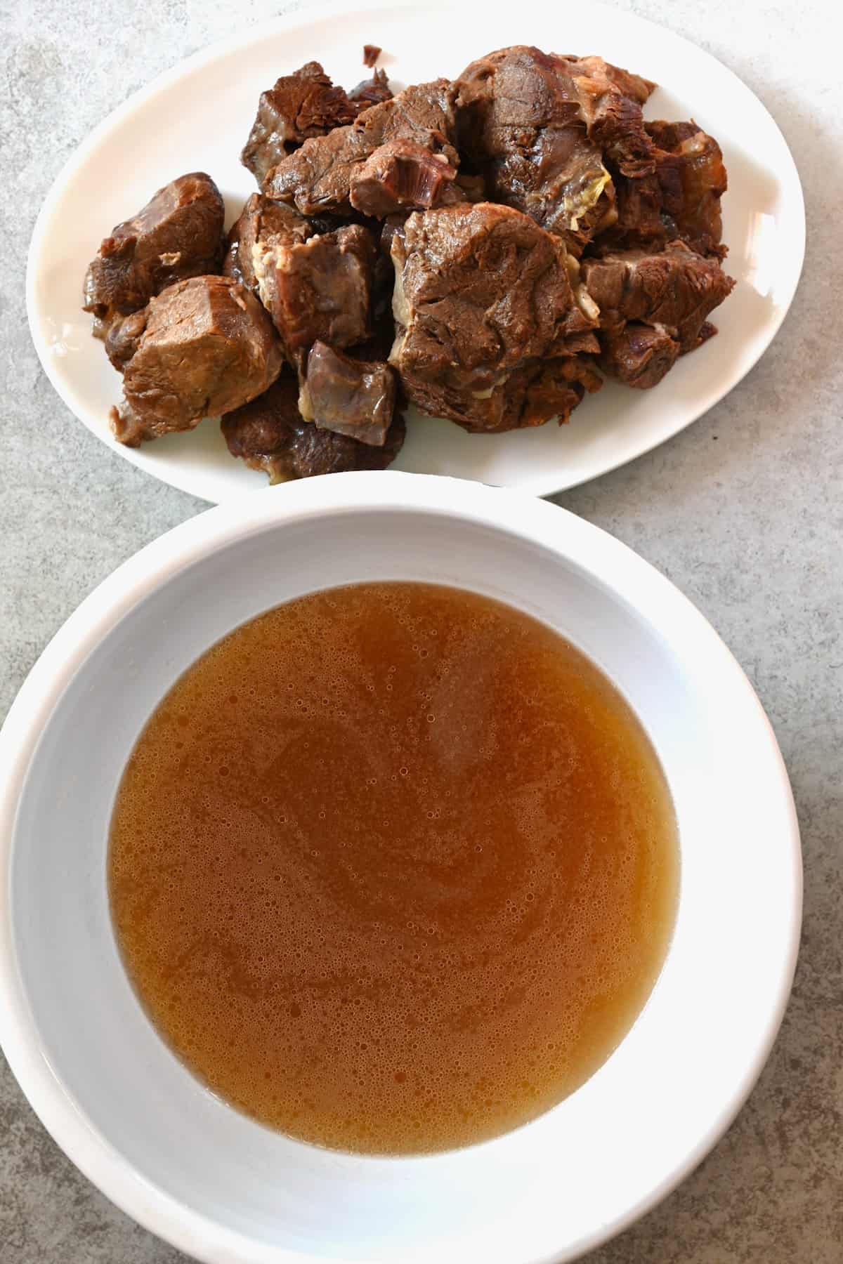 A bowl with beef broth and a plate with cooked meat