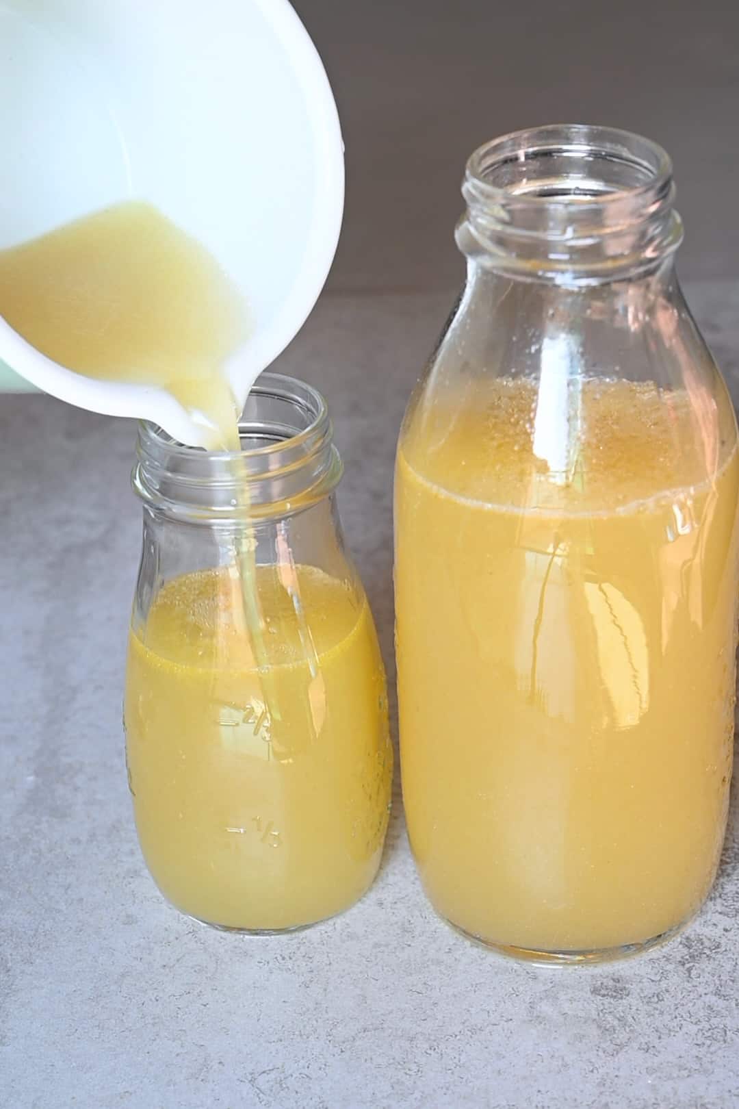 Pouring homemade chicken broth in two bottles