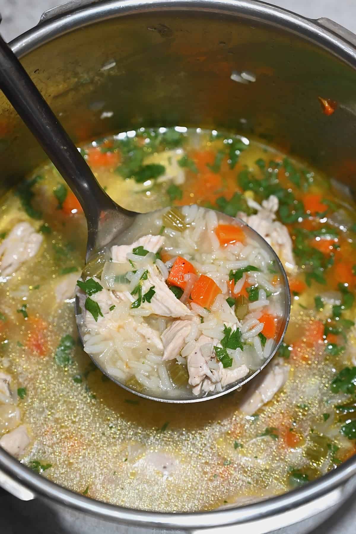 A ladle with freshly made chicken and rice soup over a pot