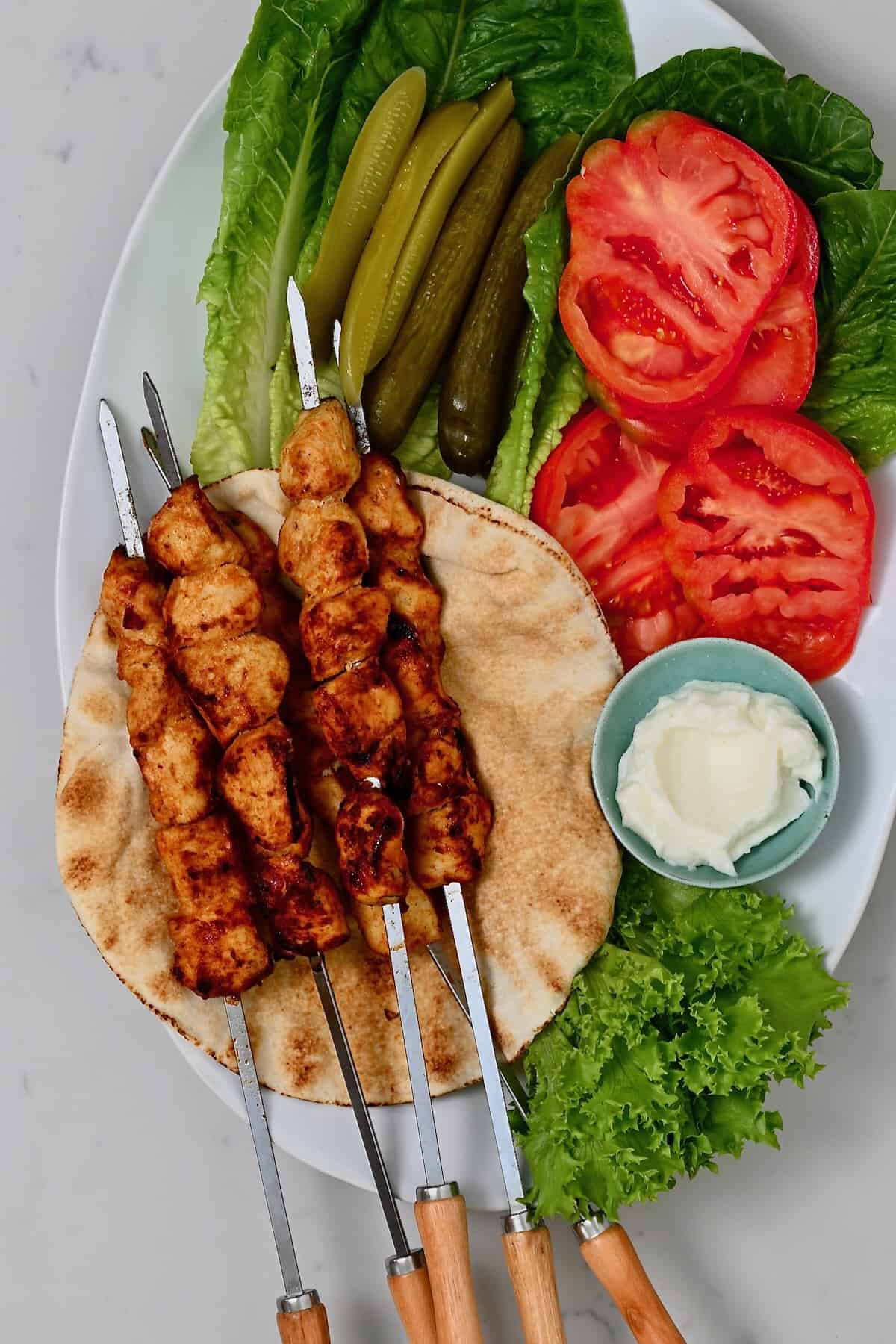 Shish tawook skewers served with tomatoes lettuce pickles and toum