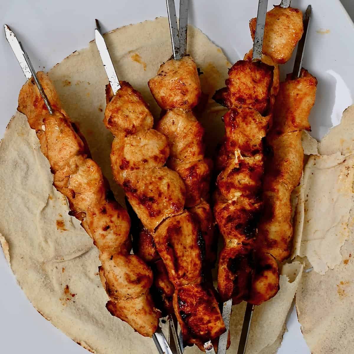 Shish tawook skewers placed over pita bread