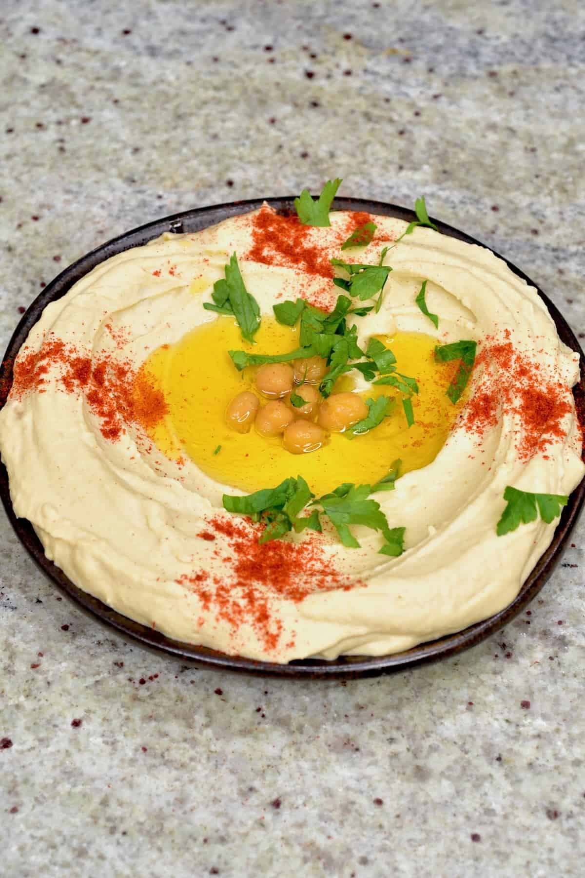 A bowl with homemade hummus topped with olive oil, parsley and paprika