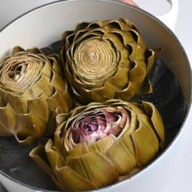 Three steamed artichoke heads in a pan