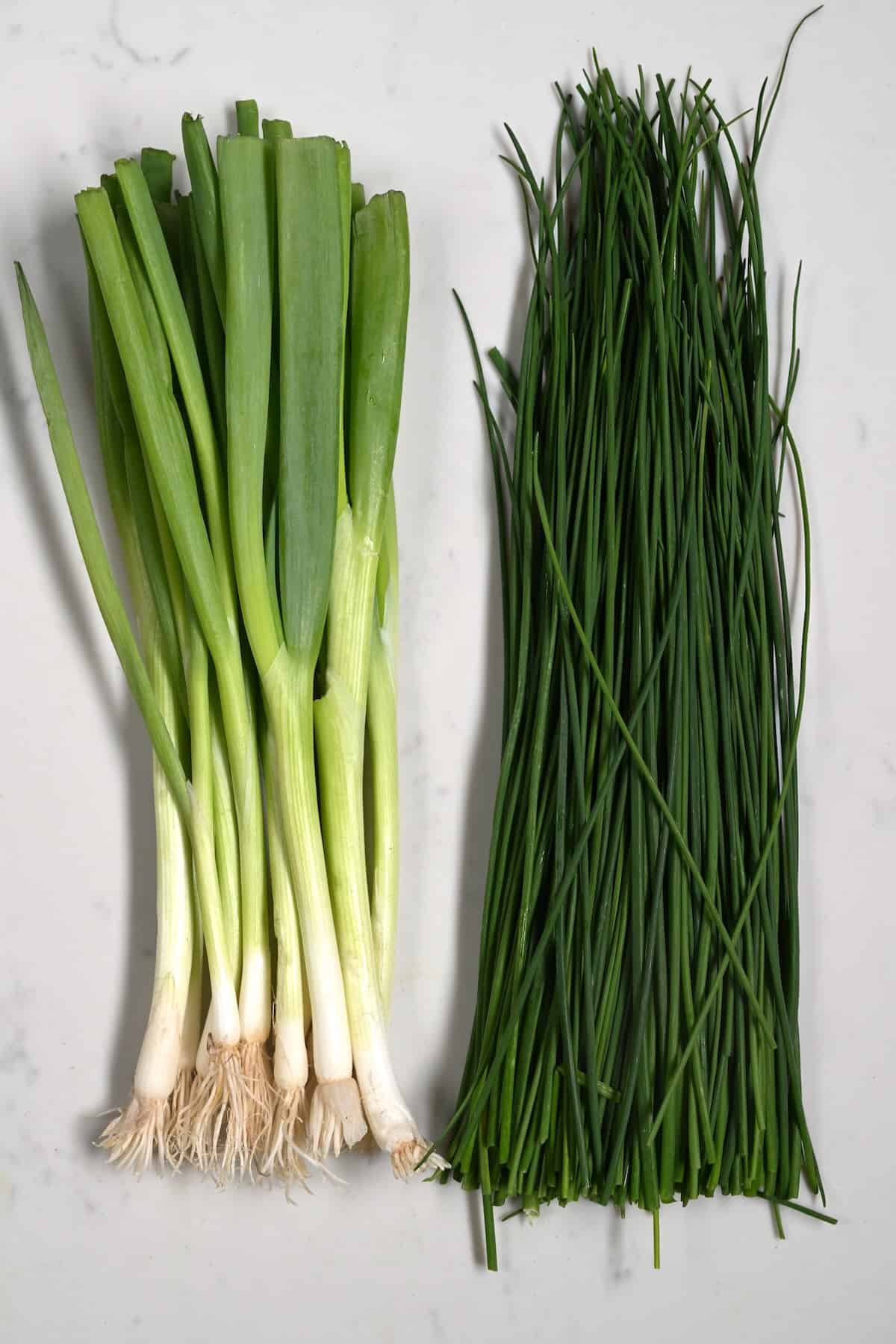 A bunch of green onions and chives on a flat surface