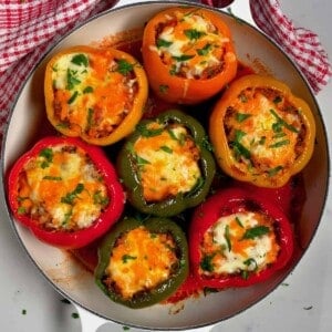 Seven stuffed bell peppers topped with melted cheese and parsley