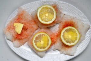Placing butter and lemon slices over cod