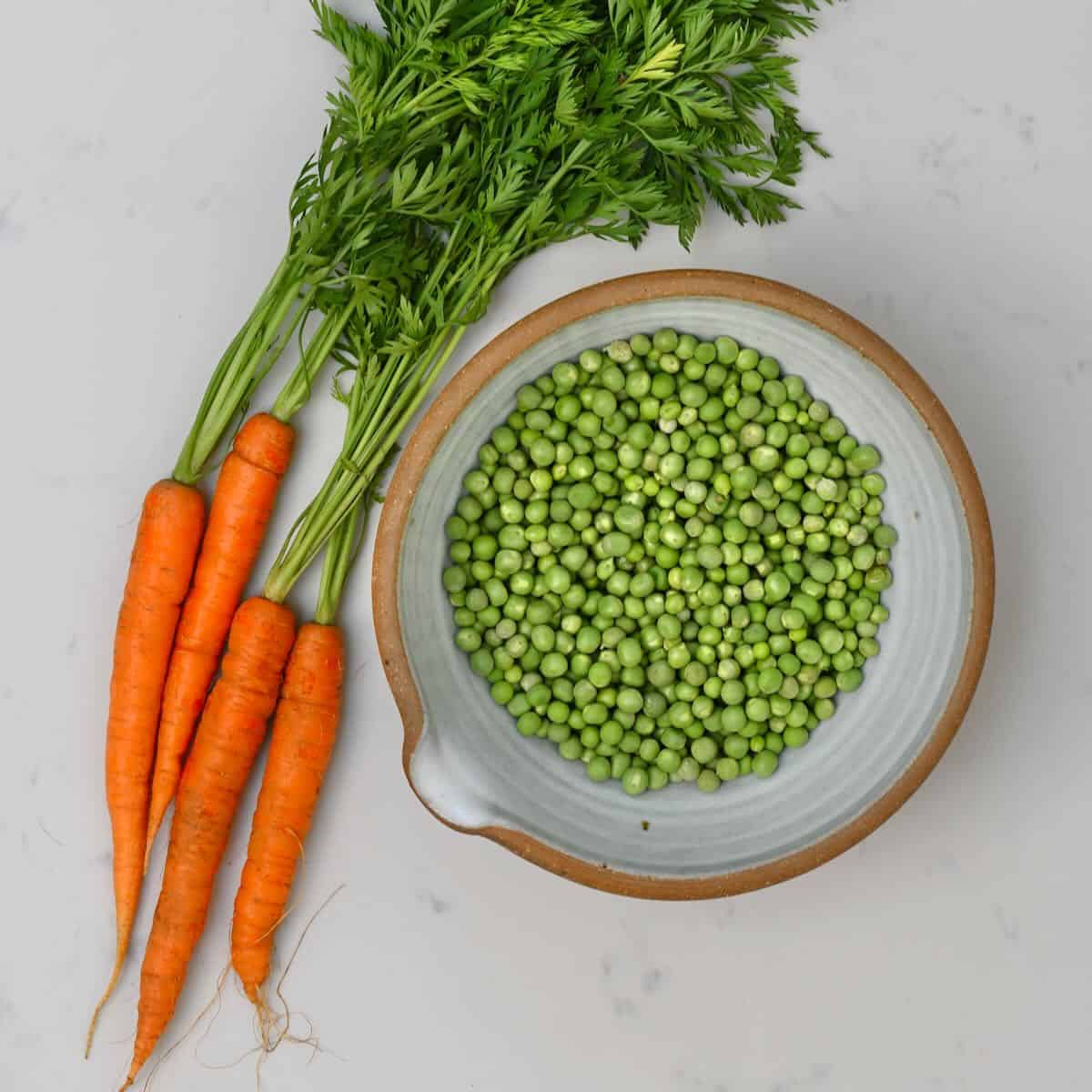 Carrots next to a bowl of peas