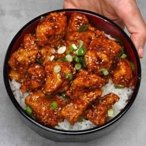 A serving of sesame chicken and rice topped with chopped scallions