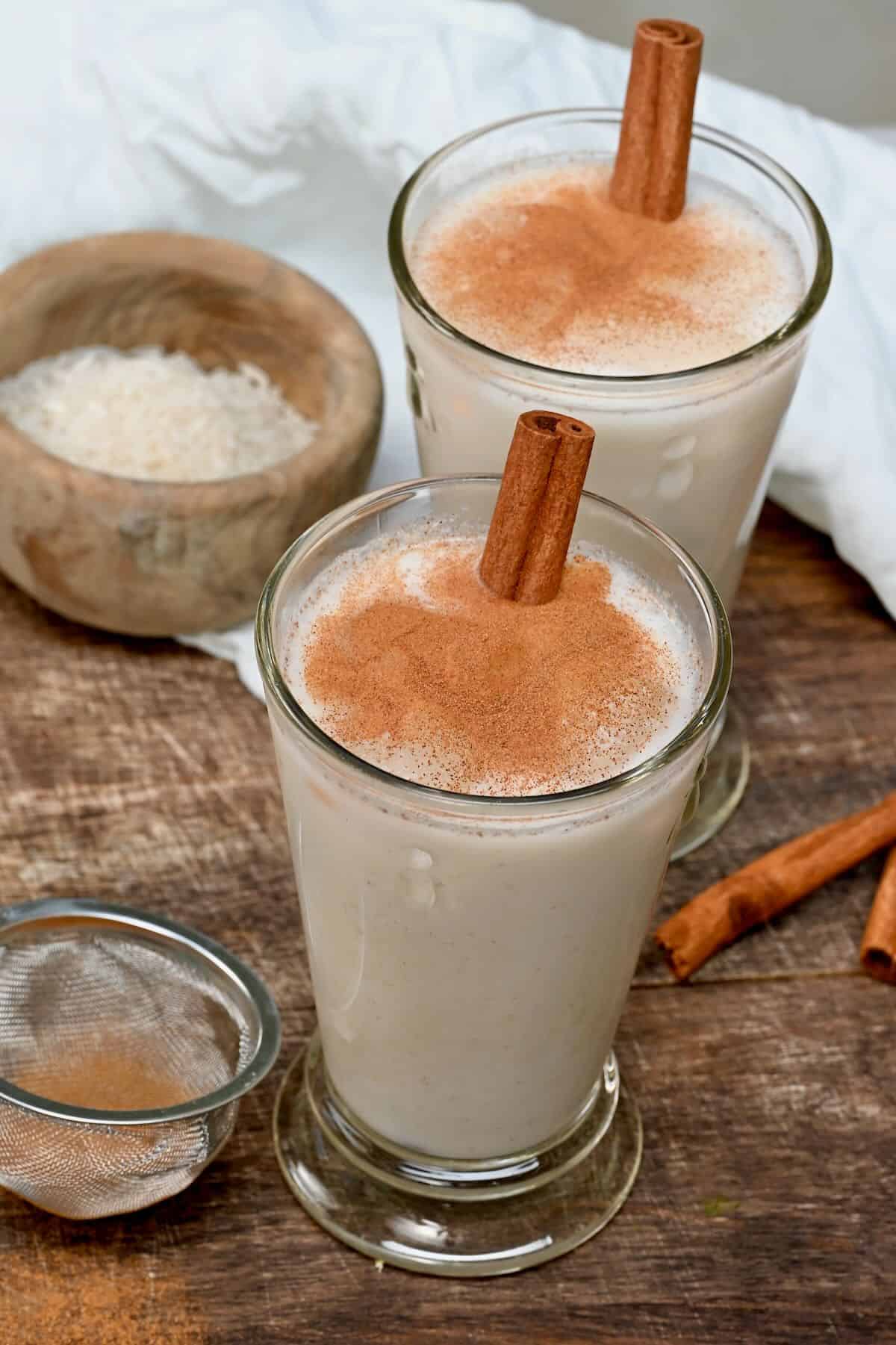 Two glasses filled with horchata and topped with cinnamon sticks and cinnamon powder