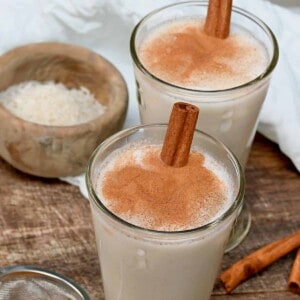 Two glasses filled with horchata and topped with cinnamon sticks and cinnamon powder