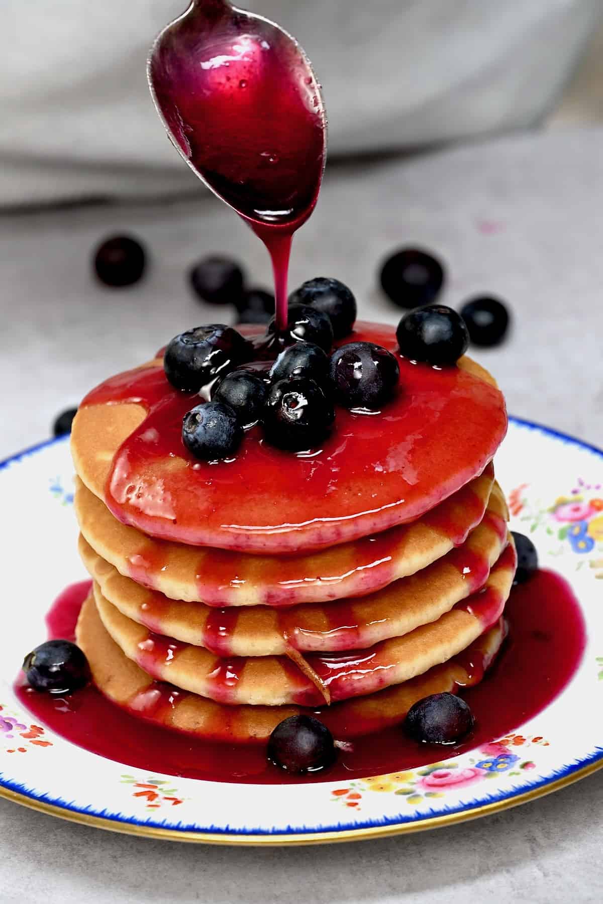 Spooning homemade blueberry syrup over a stack of pancakes