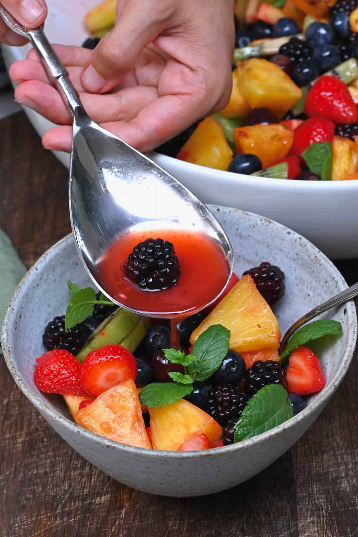 Adding some dressing over fruit salad in a bowl