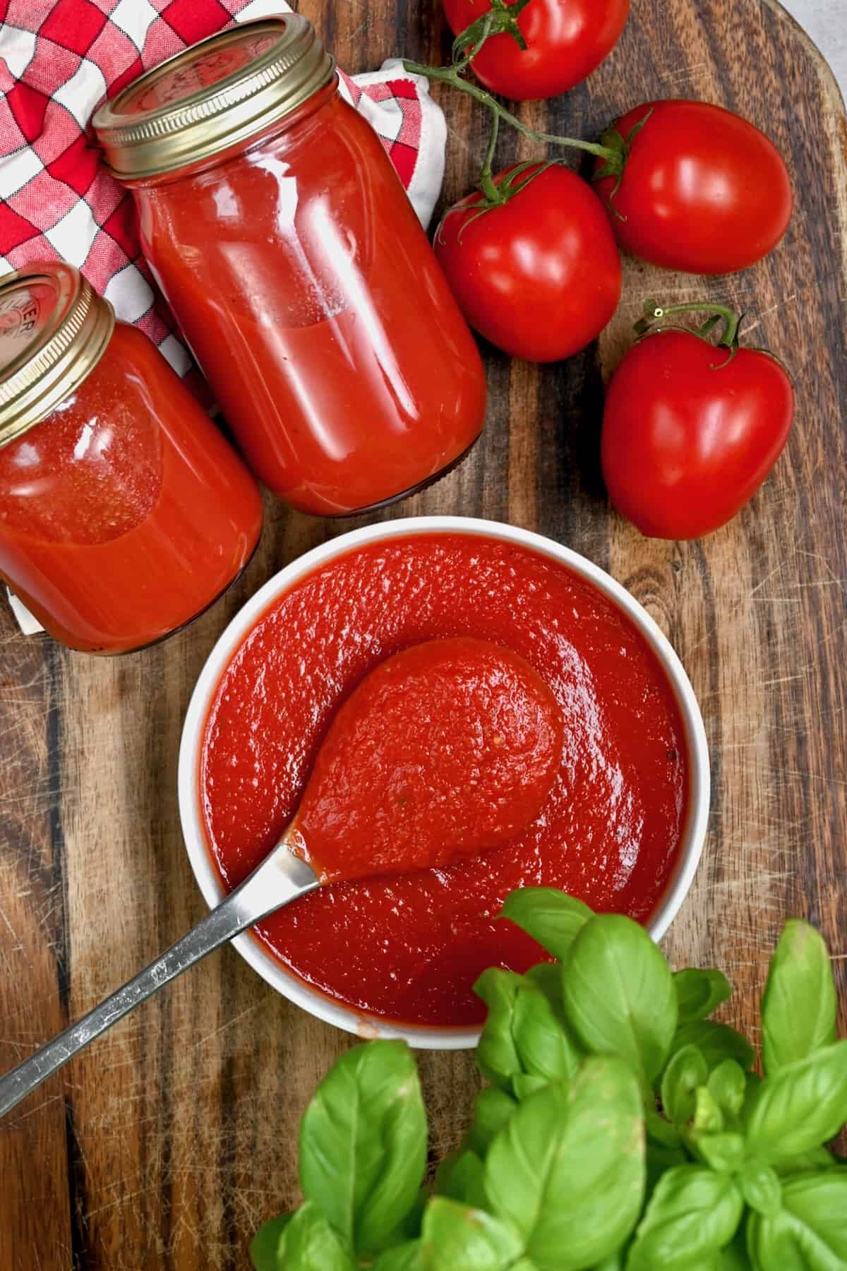 Homemade pizza sauce in a bowl and in jars next to tomatoes