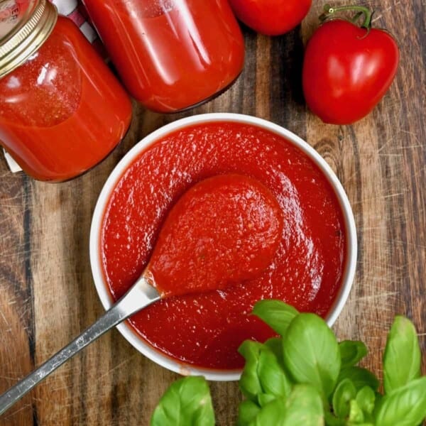Homemade pizza sauce in a bowl and in jars next to tomatoes