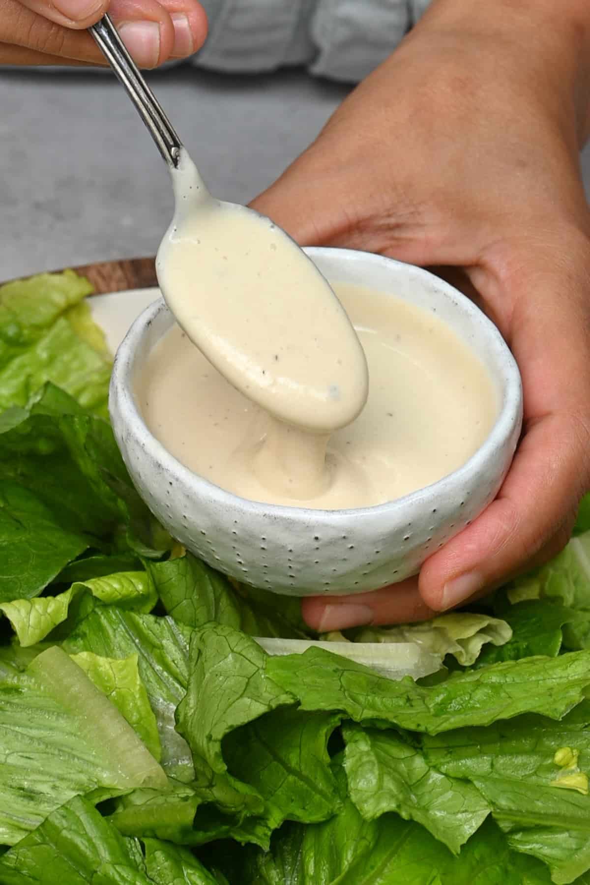 Adding a spoonful of homemade Caesar dressing to salad
