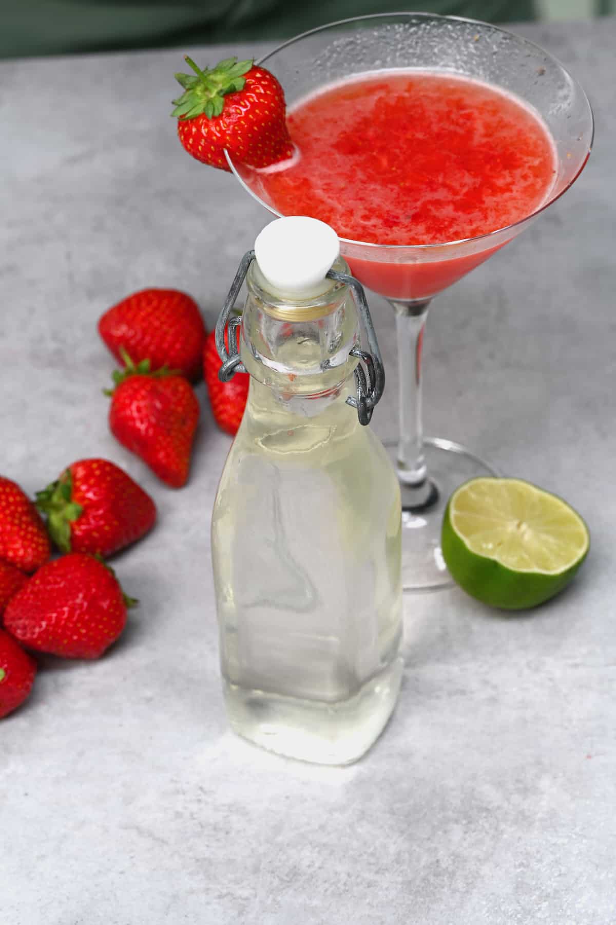 A bottle of simple syrup and a strawberry cocktail