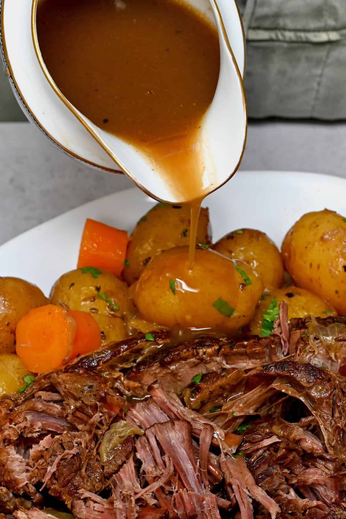 Pouring gravy over chuck roast and potatoes