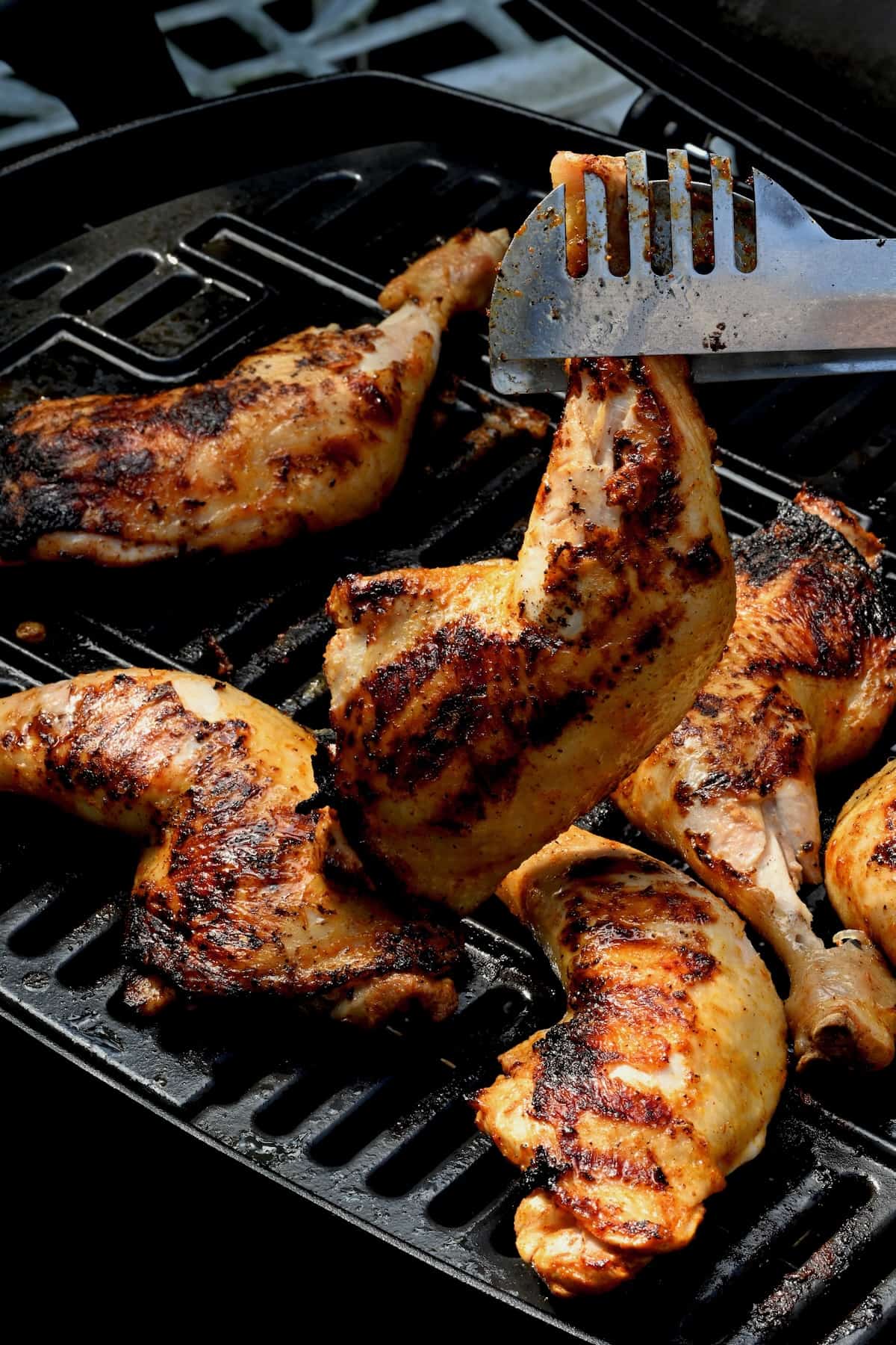 Grilled chicken quarter being removed from the grill