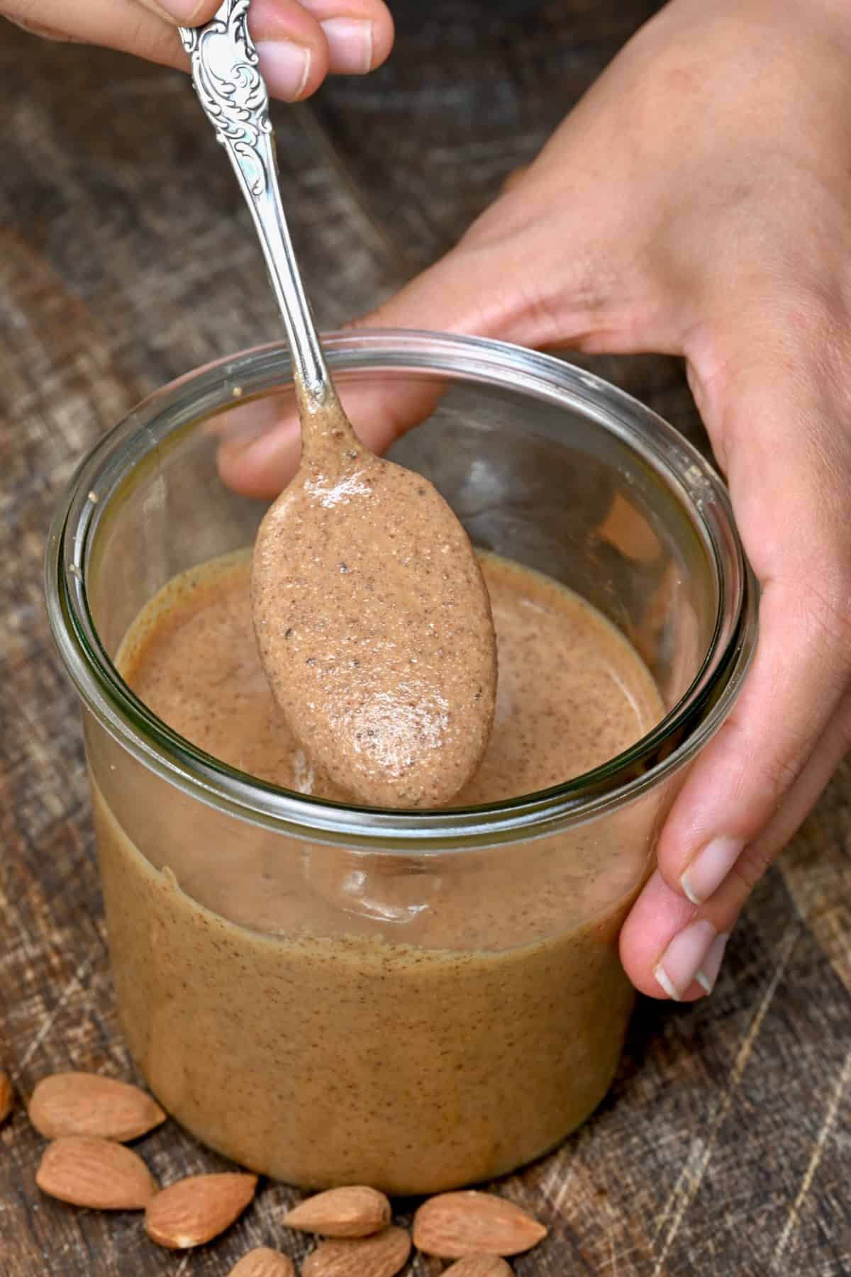 A spoonful with homemade almond butter over a jar