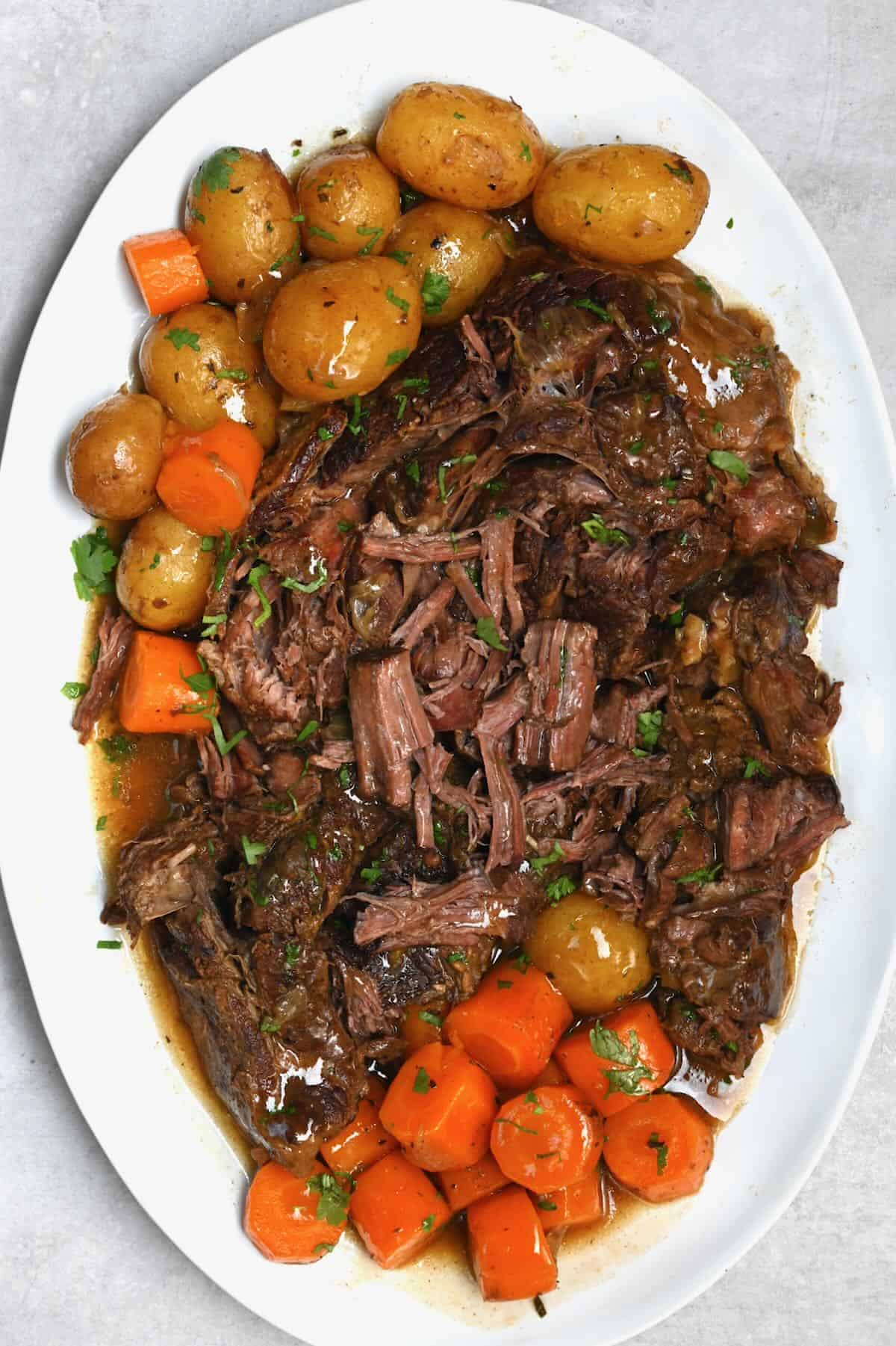 Crock pot roast dinner on a white plate with carrots and potatoes
