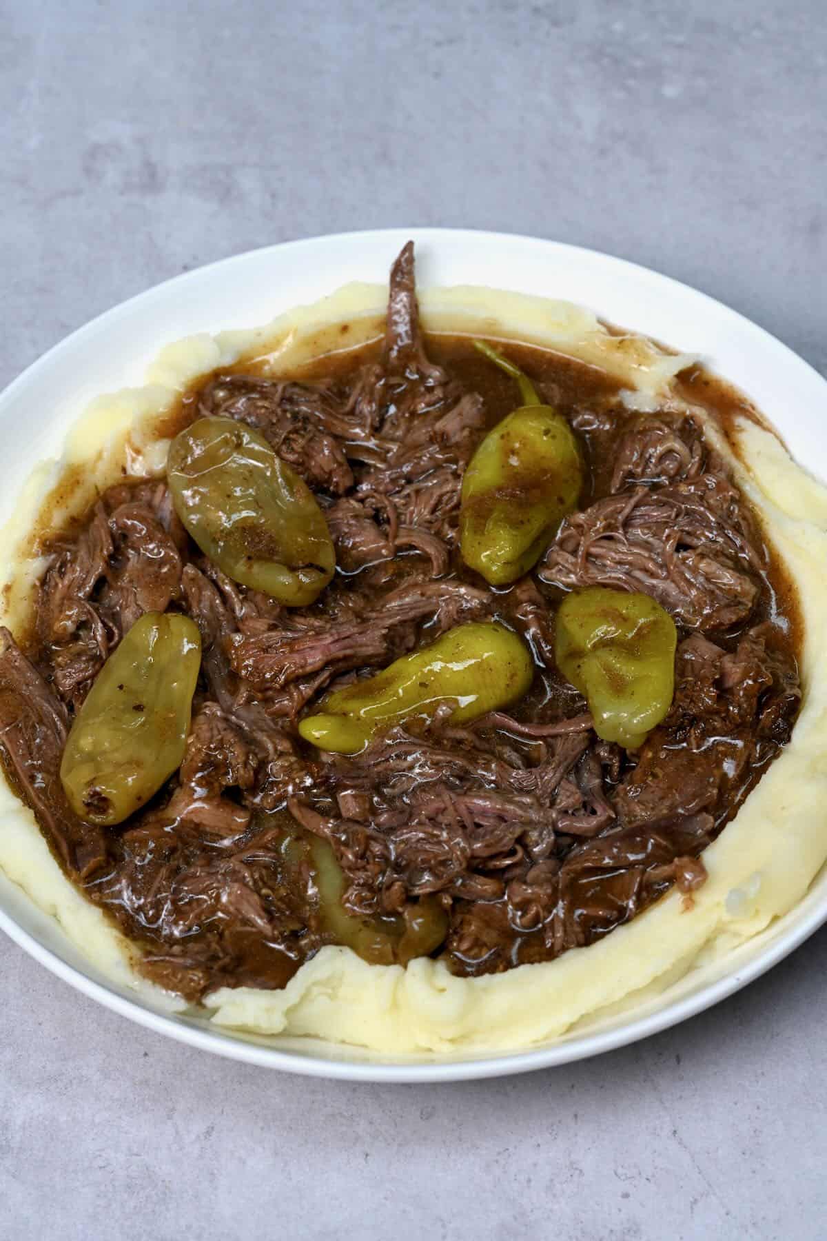 Mississippi pot roast on top of mashed potato on a white plate
