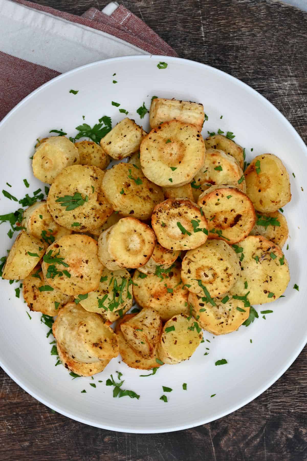 Roasted Parsnips on a white plate with sprinkle of parsley