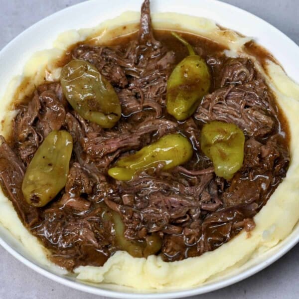 close up of Mississippi pot roast on top of mashed potato on a white plate