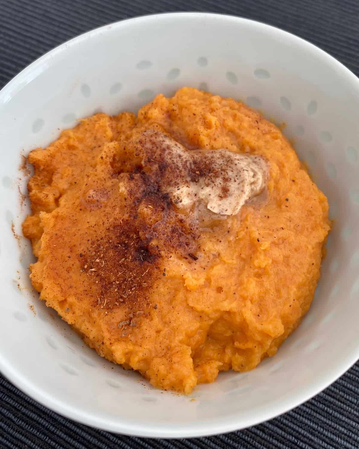 Mashed sweet potatoes topped with butter and cinnamon in a bowl