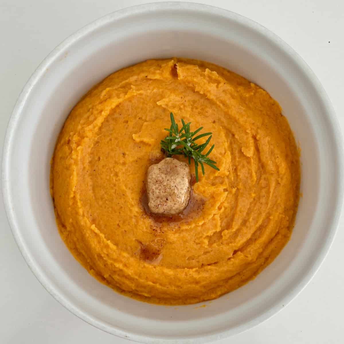 Mashed sweet potatoes topped with butter and rosemary in a bowl