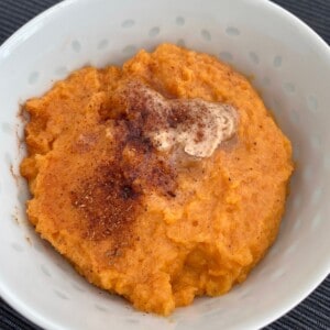 Mashed sweet potatoes topped with butter and cinnamon in a bowl