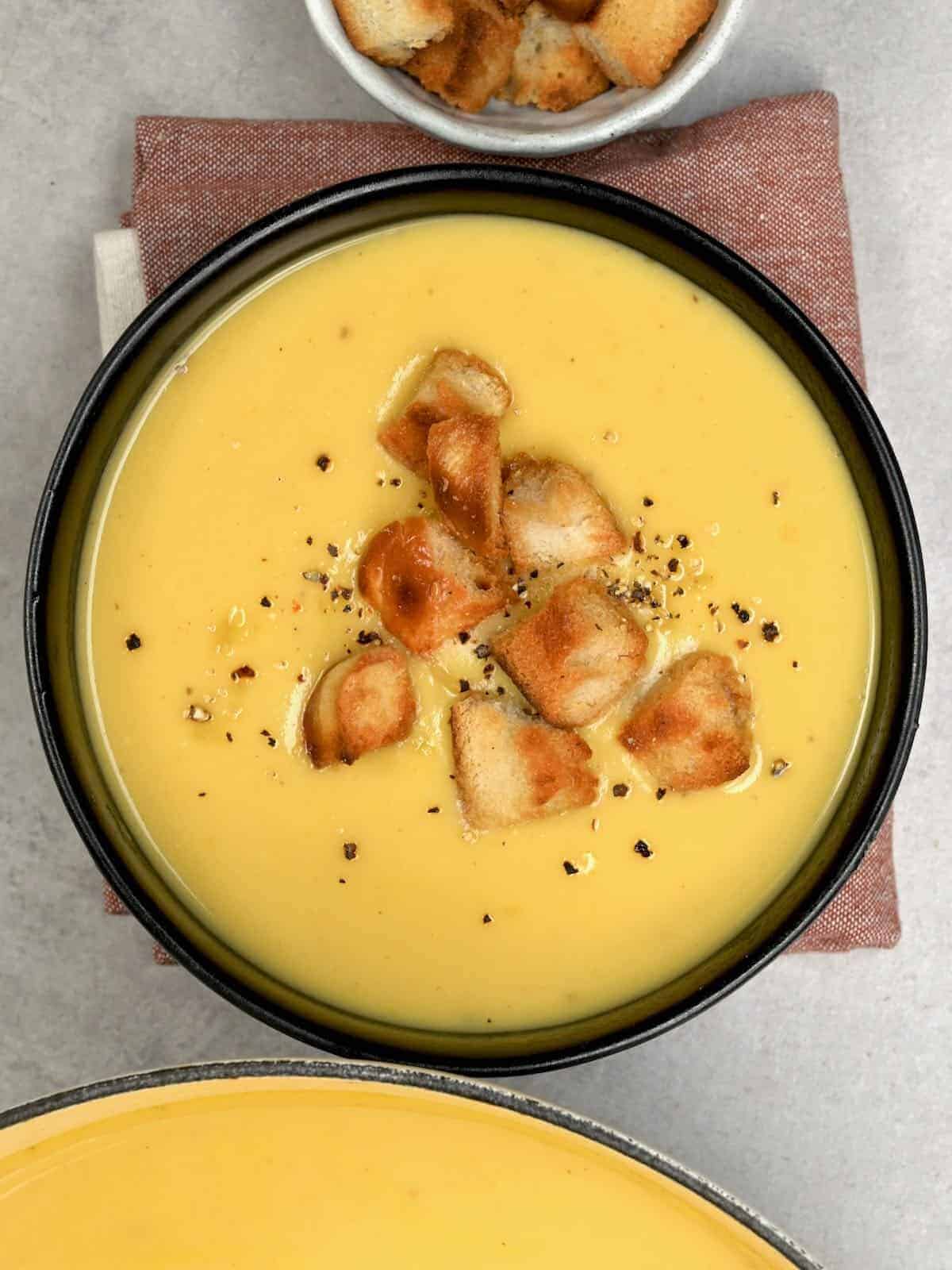 Parsnip Soup in a black bowl with croutons on top