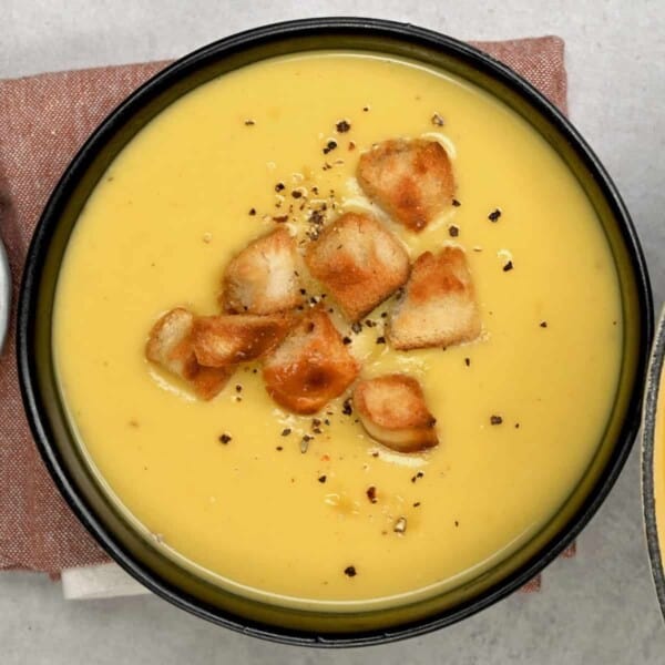 Parsnip Soup in a black bowl with croutons on top