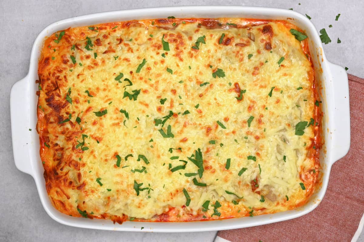 Baked lasagna in a dish, garnished with finely chopped parsley leaves.