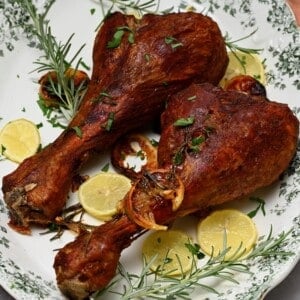 Two roasted turkey legs on a plate with onion and rosemary