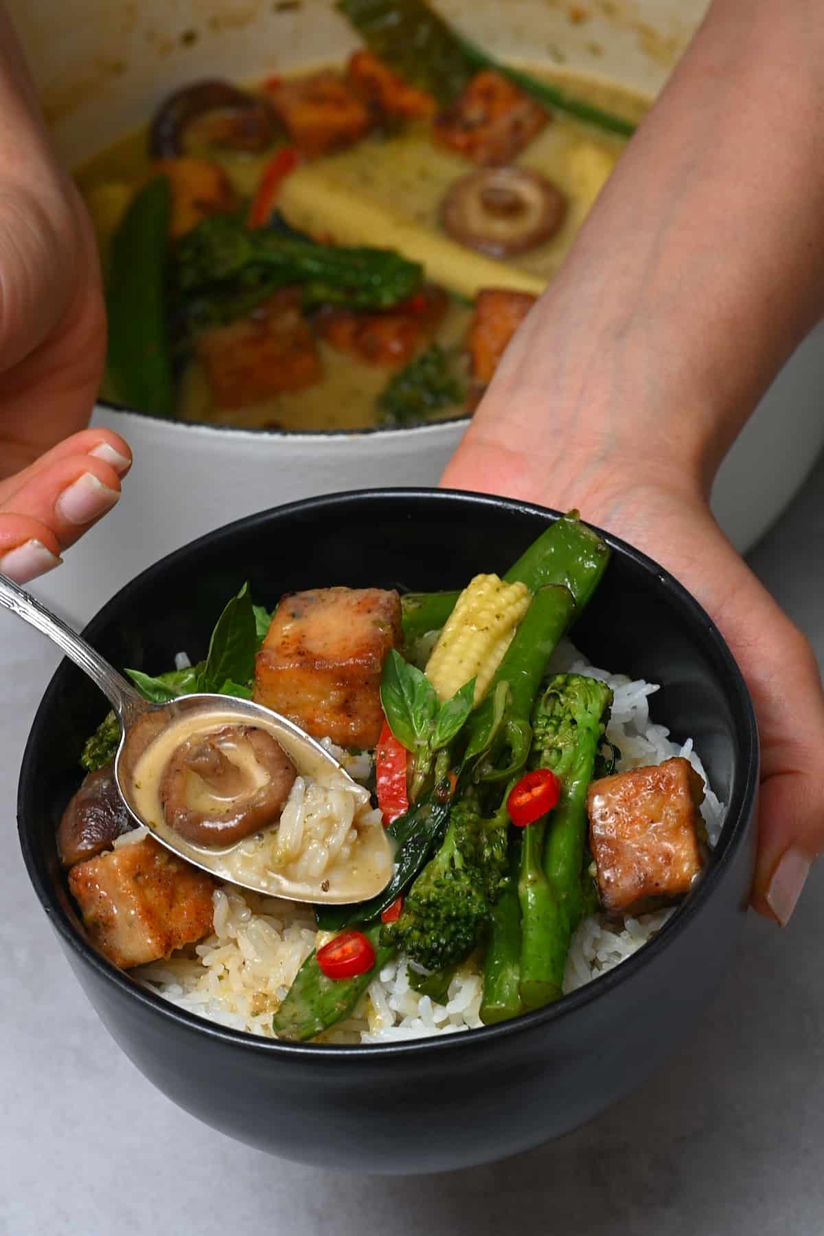 Vegetarian green curry served in a black bowl with rice.