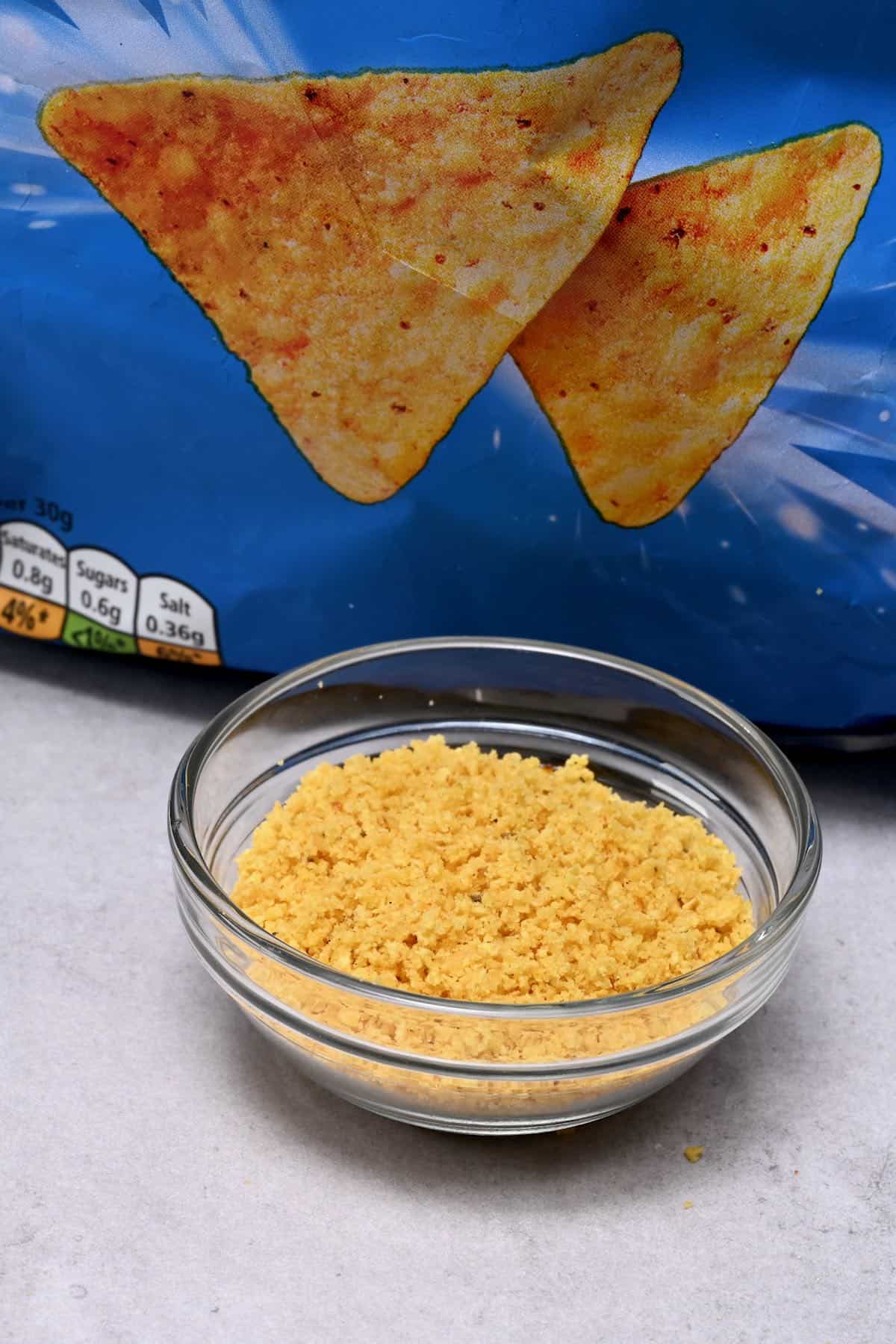 crushed tortilla chips in a glass bowl with tortilla chips bag behind