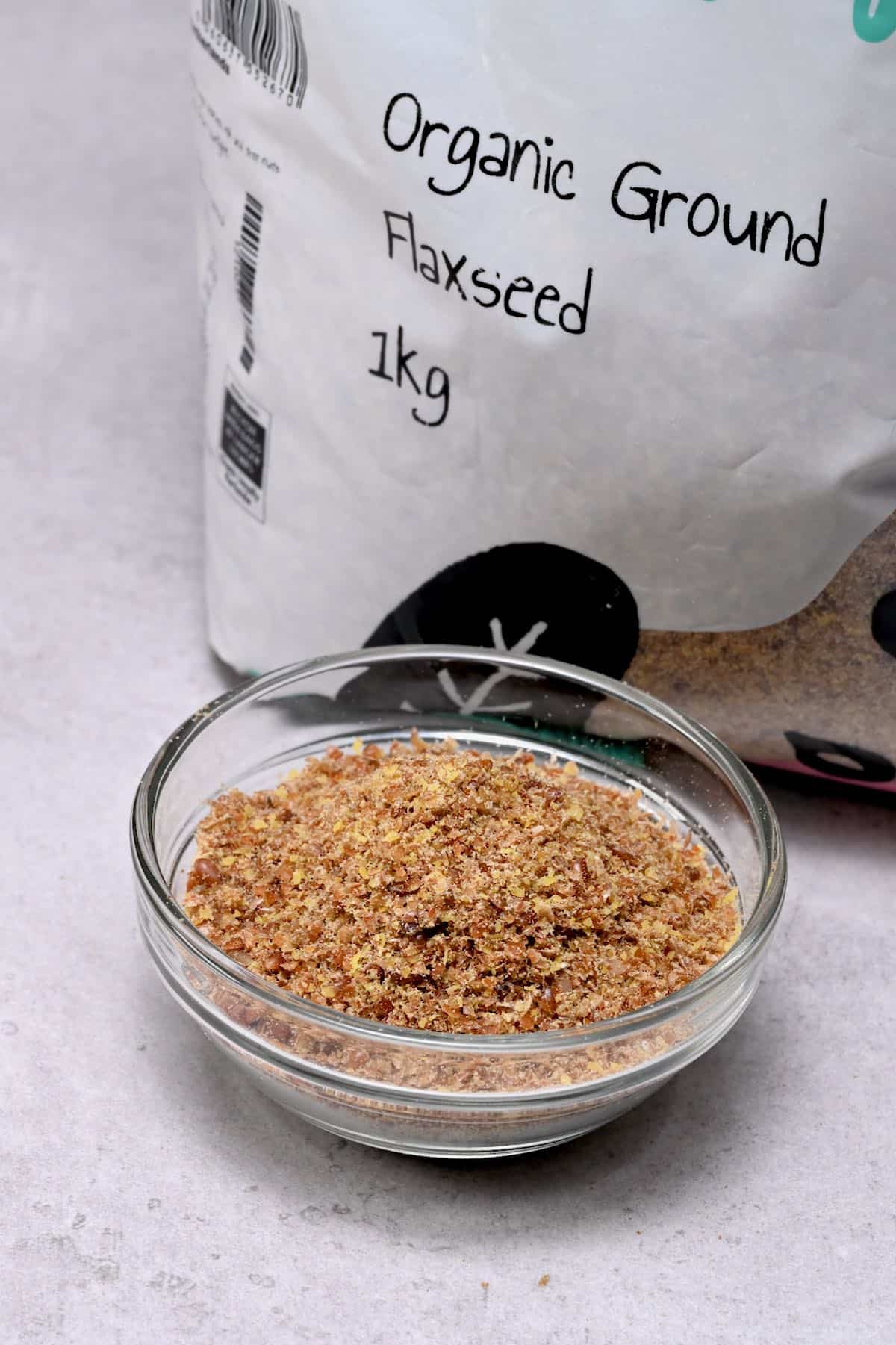 ground flaxseed in a glass bowl with flaxseed bag behind
