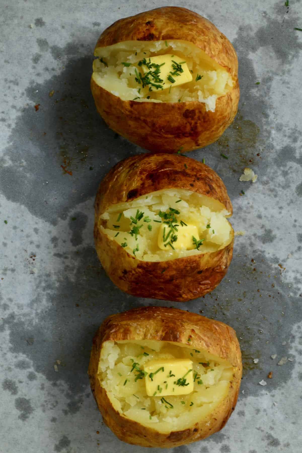Three baked potatoes with some melted butter topped with chives
