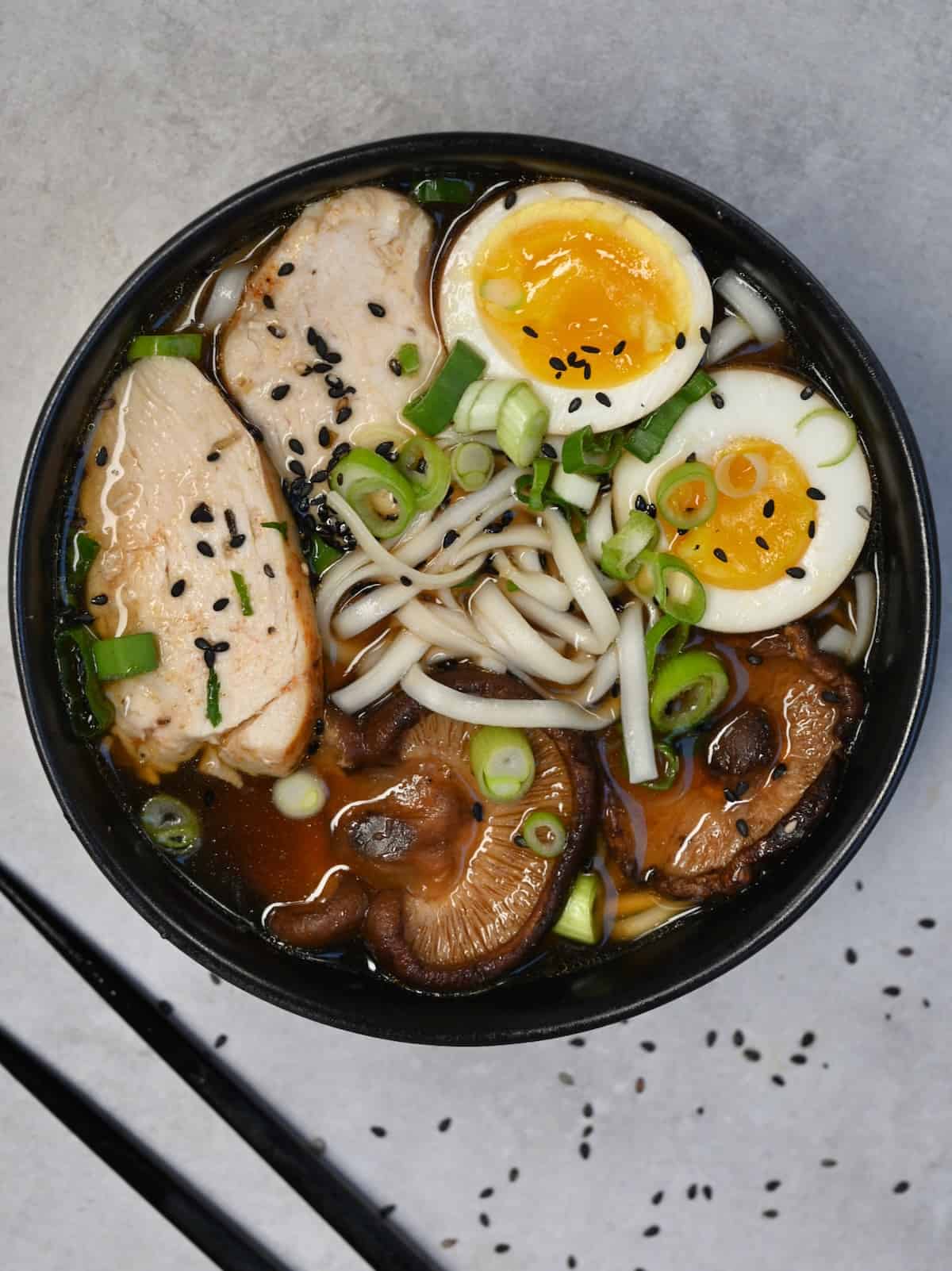 A bowl of homemade chicken ramen with ramen eggs topped with black sesame seeds and spring onion