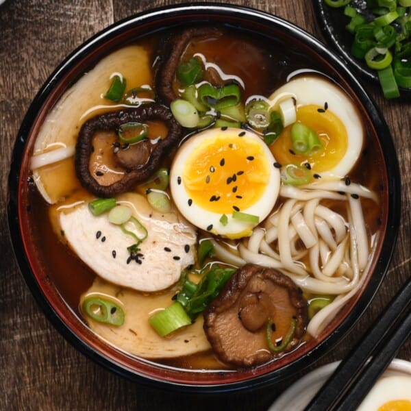 A bowl of homemade chicken ramen with ramen eggs topped with black sesame seeds and spring onion