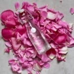 A clear bottle of rose water placed on a bed of rose petals.
