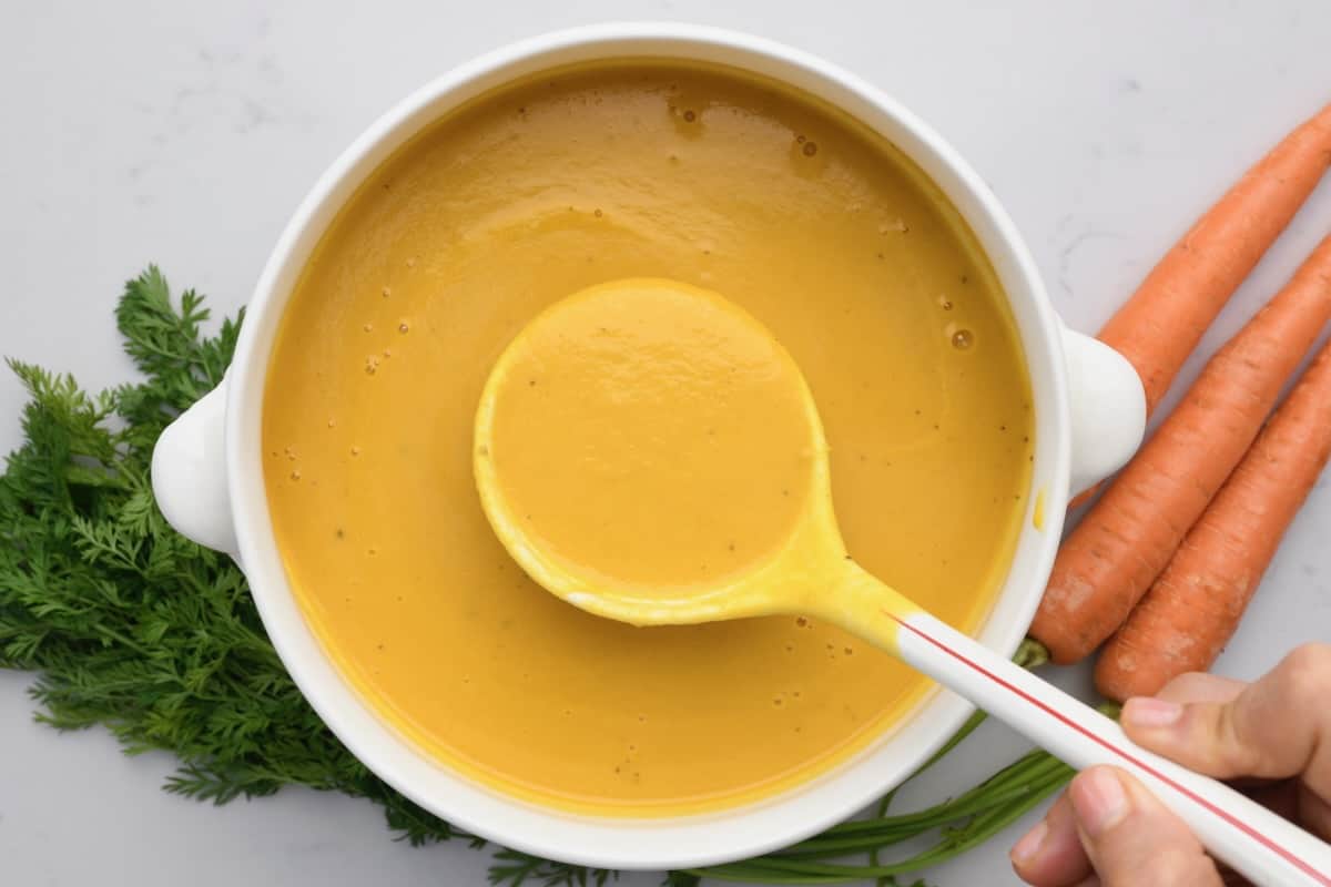 A ladle spooning carrot soup over a serving bowl