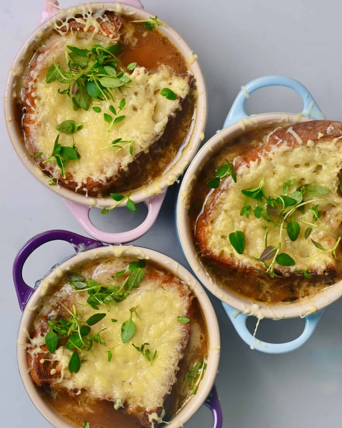 Three small bowls with French onion soup topped with cheesy toast