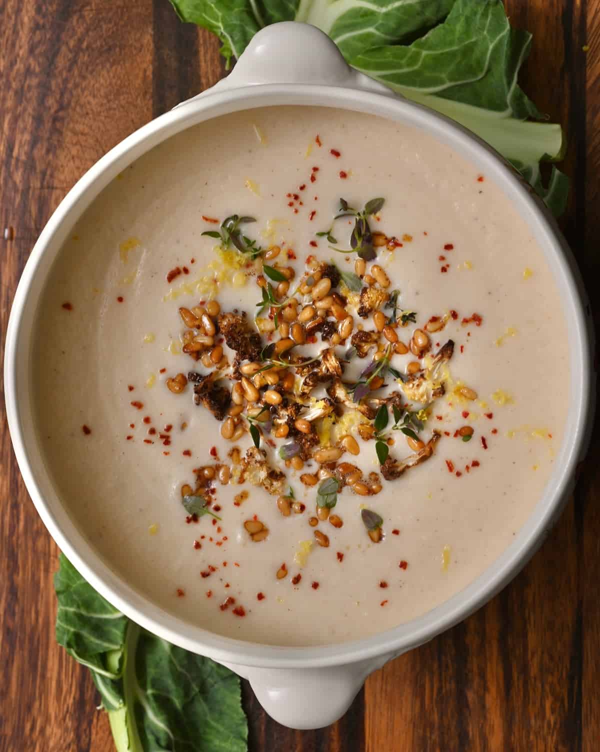 A bowl of homemade cauliflower soup topped with toasted pine nuts and lemon zest