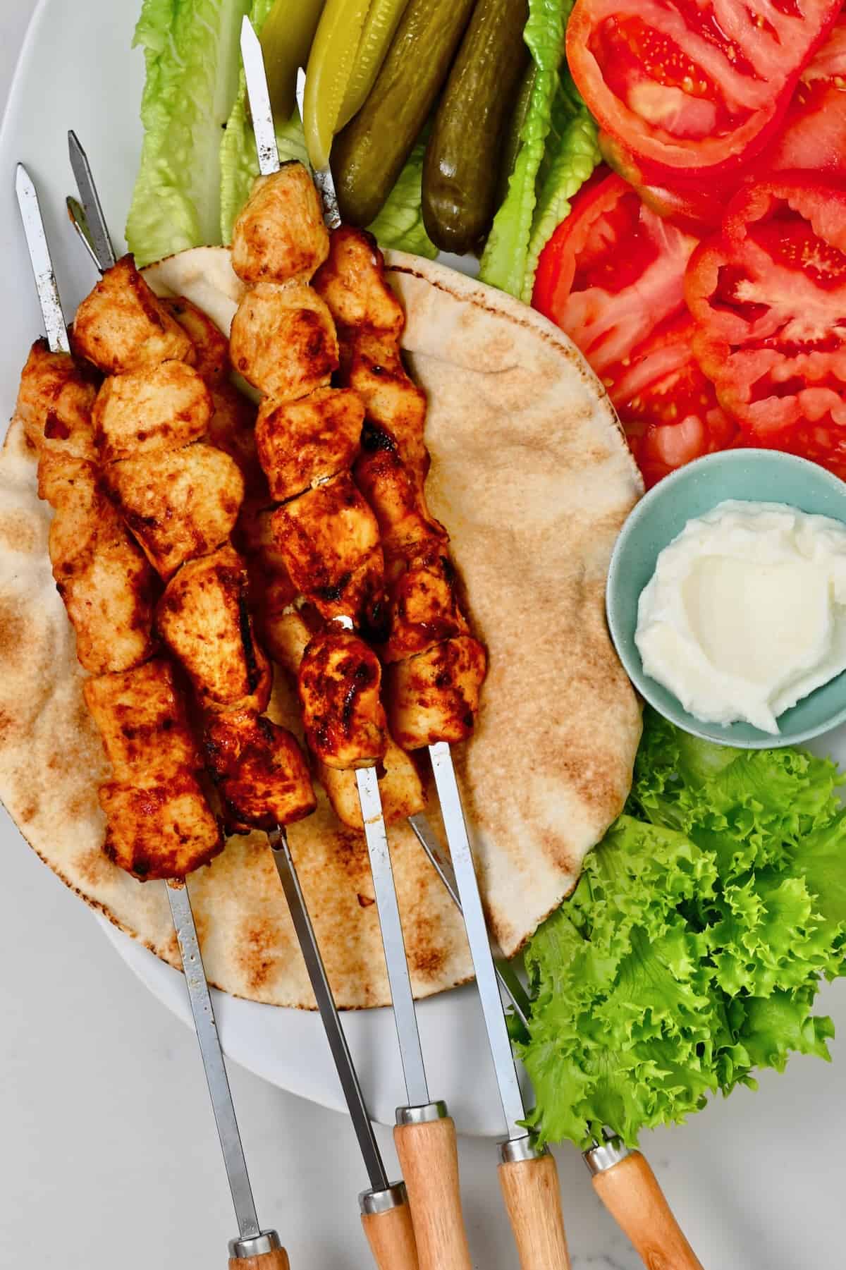 Homemade chicken shish tawook served alongside tomatoes, tour and lettuce