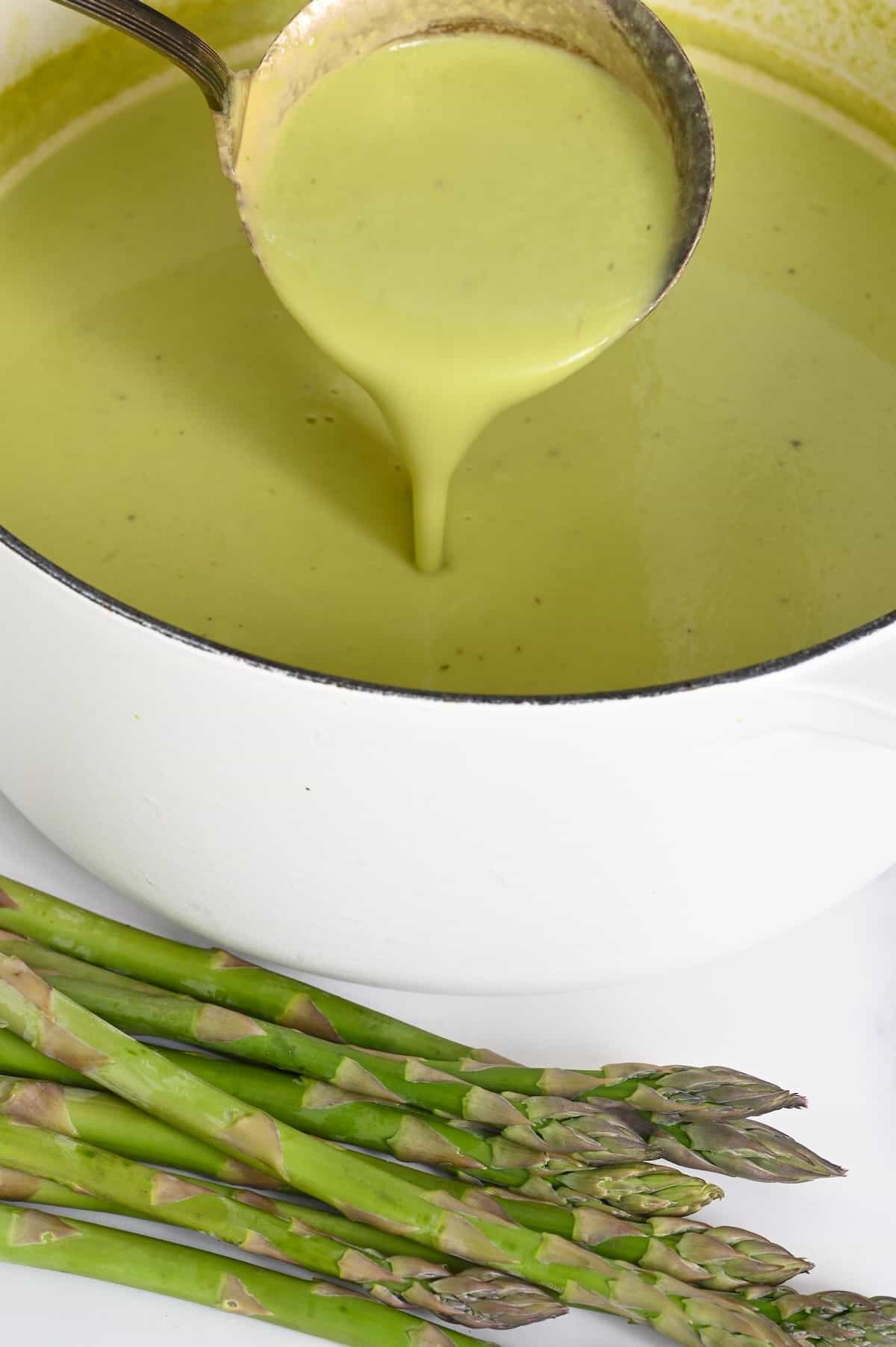 A ladle pouring asparagus soup in a saucepan
