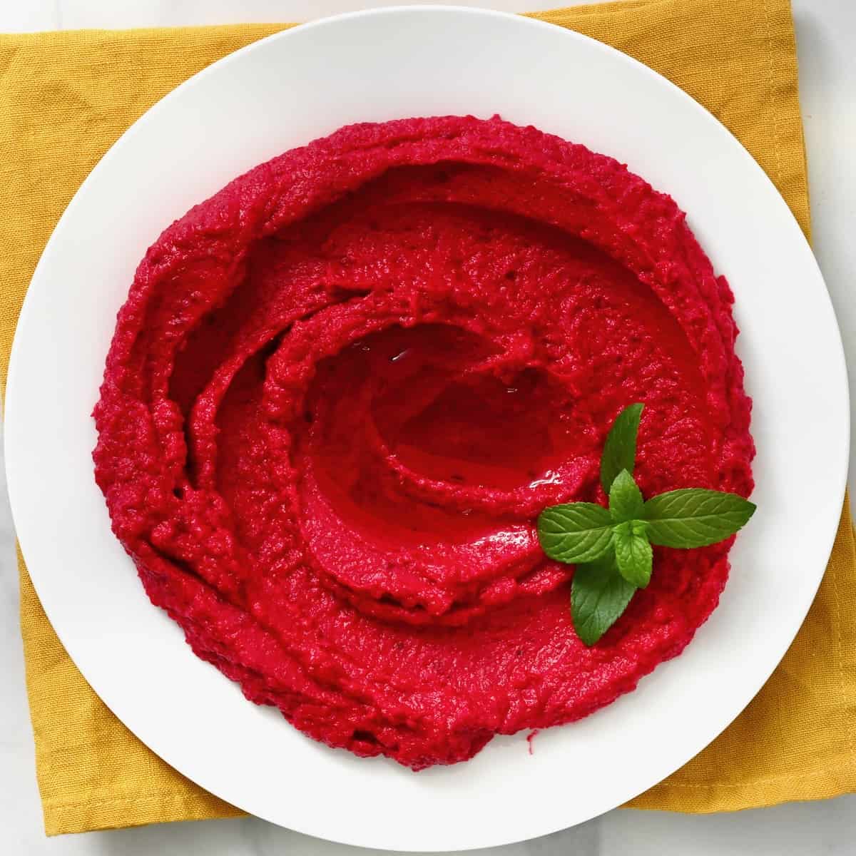 A serving plate with homemade beet hummus topped with mint leaf